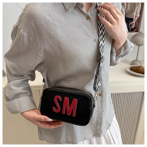 Close-up of black crossbody bag with red SM letter applique and wide woven shoulder strap