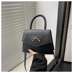 Detail of classic black leather crossbody bag featuring a golden bow metal clasp and handle