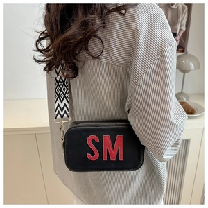 Detail of black crossbody bag with red SM letter patch and wide geometric strap