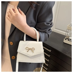 Detail view of white crossbody bag with golden bow hardware worn by a model
