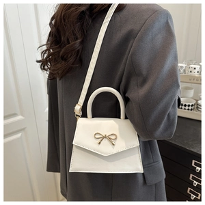 White square handbag with golden bow buckle shown on model wearing a grey-blue blazer