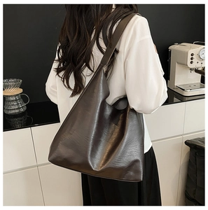 Detail shot of a large matte leather tote bag worn by a model in an urban office setting