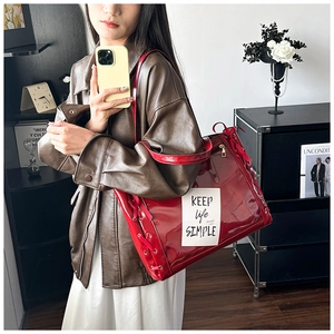 Detail of red patent leather tote bag featuring side lace-up design and text patch label