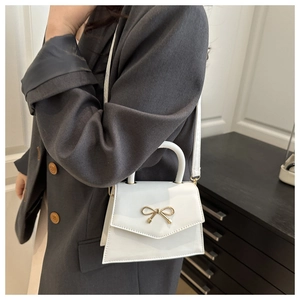 Detail of white leather handbag featuring a gold bow buckle worn with a grey blazer