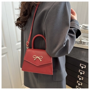 Detail of red crossbody bag with golden bow clasp worn over a gray fashion blazer