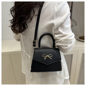 Detail of a black leather crossbody bag featuring a golden bow buckle and slim strap