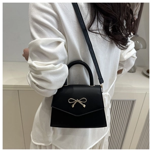 Detail of elegant black envelope bag with golden bow clasp and top handle on a model