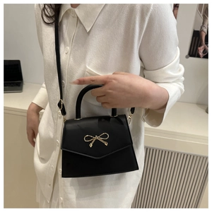Detail shot of a black crossbody bag with a signature golden metallic bow decoration