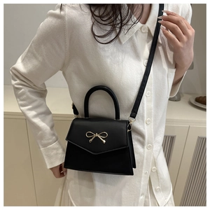 Detail of black PU leather handbag with golden metal bow clasp and adjustable strap