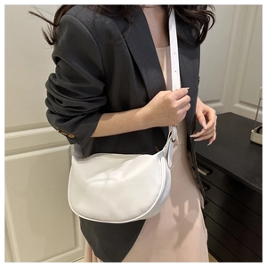 White semi-circle crossbody bag with adjustable strap worn on the shoulder by a model