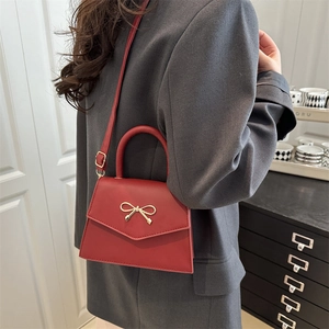Elegant burgundy leather top handle crossbody bag with gold bow clasp on a grey coat