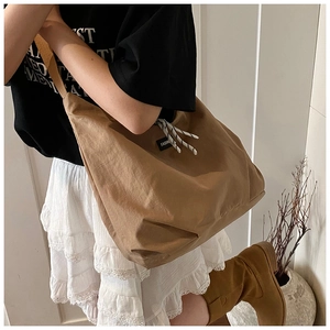 Detail of a large khaki tote bag with fashion tag and striped drawstring on a model