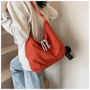 Detail of large orange canvas tote bag with decorative striped knot and zipper on strap