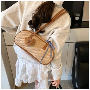 Detail of woven straw shoulder bag with brown leather trim and cute plush bear charm