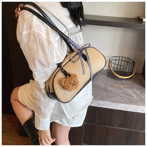 Detail of woven straw shoulder bag with black leather trim, ribbon bow and bear charm