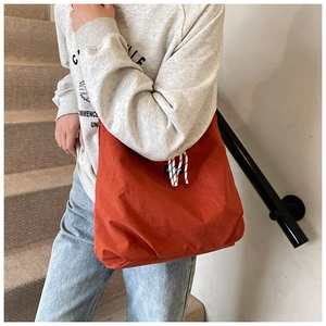 Detail of orange canvas tote bag with fashion label and striped drawstring accent