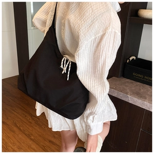 Detailed side view of large black canvas shoulder bag with fashion label and braided cord