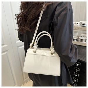 Detail of white leather handbag featuring knotted handles and gold metal eyelets