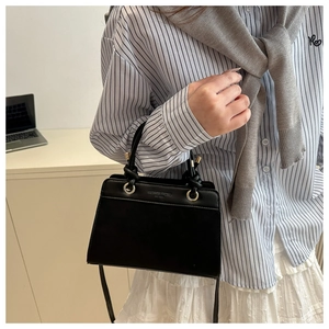 Detail of black faux leather tote featuring knotted handle and gold metal ring buckle
