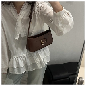 Dettaglio della borsa a mezzaluna in pelle marrone scuro con fibbia dorata su modella