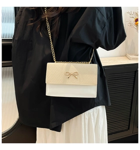 Détail du sac à rabat crème avec nœud doré et surface à texture sergé de haute qualité
