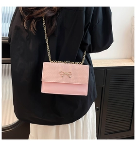 Détail du sac bandoulière rose avec boucle nœud doré et chaîne sur une mannequin