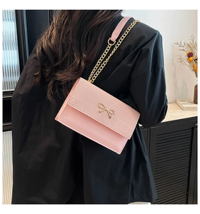 Lifestyle shot of a pink crossbody chain bag with a decorative golden bow buckle