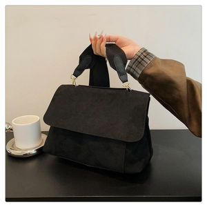 Detail of black suede briefcase with woven shoulder strap and golden metal hooks