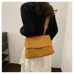 Detail of mustard suede crossbody bag with wide shoulder strap worn by a model