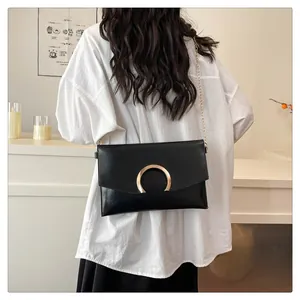 Detail of a black leather envelope bag featuring a large gold semi-circular metal buckle