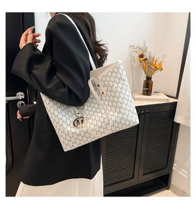 Close-up of white tote bag featuring black M monogram print and gold metal logo charm