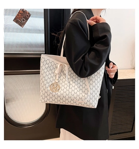 Detail of large beige tote bag with grey M pattern and gold metal pendant