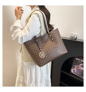 Detail of coffee brown tote bag with M monogram pattern and golden metal pendant