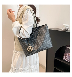 Chic black tote bag with silver M pattern and gold logo pendant shown on a model