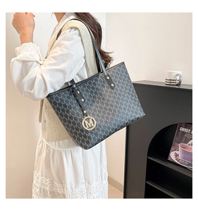 Detail of black tote bag featuring white M pattern and gold M charm on shoulder