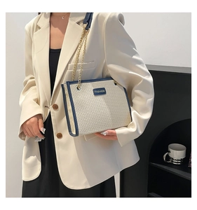 Détail du sac fourre-tout crème avec bordure en cuir bleu marine et chaîne dorée