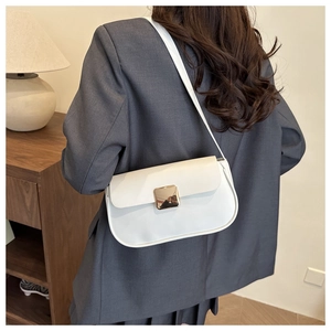 Sac bandoulière blanc chic avec boucle dorée porté par un mannequin dans une pièce