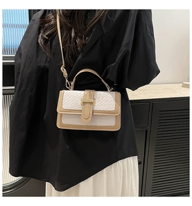 Detail of white woven crossbody bag with brown leather trim and golden metal clasp on a model