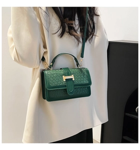 Detail of dark green textured crossbody bag with gold H-buckle on beige blazer