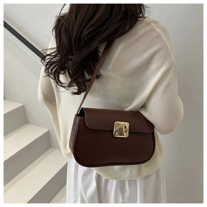 Sac à bandoulière marron minimaliste avec boucle dorée porté sur un pull en maille beige