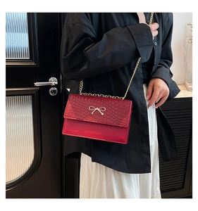 Close-up of red woven texture crossbody bag with gold bow clasp and chain strap