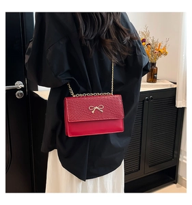 Detail of red stone texture shoulder bag with gold bow decoration on model