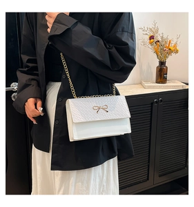 Close-up of white crossbody bag with crocodile texture and gold bow metal buckle