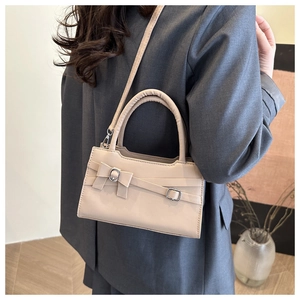 Detail of a minimalist beige crossbody bag with a large bow and silver metal buckle