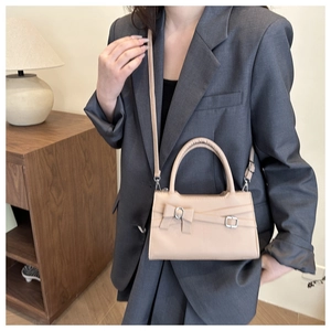 Detail of beige square handbag with bow accent and crossbody strap on grey blazer
