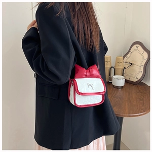 Detail of white crocodile texture mini bag with red bow and silver metal charm