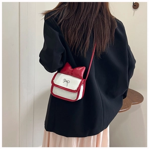Detail of a mini crossbody bag featuring a red bow and white faux crocodile texture
