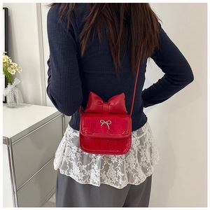 Detail of red mini crossbody bag with crocodile pattern and decorative bow on model's waist
