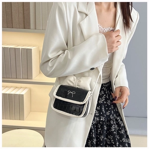 Detail of a mini black and white crossbody bag with a large bow and crocodile pattern