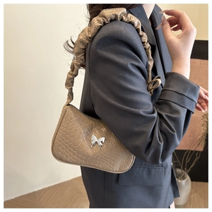 Détail du sac à bandoulière en motif crocodile kaki avec boucle papillon argentée et sangle plissée